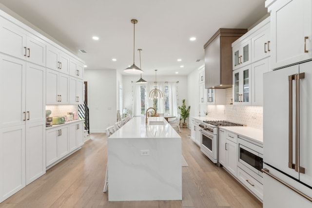 kitchen with a center island with sink, light wood-type flooring, decorative light fixtures, and high end appliances