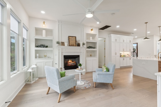 living room with ceiling fan, light hardwood / wood-style floors, built in shelves, and a tiled fireplace