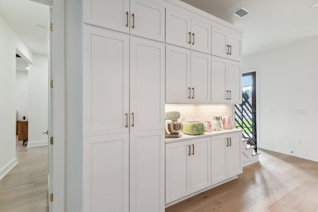 bar featuring decorative backsplash, light hardwood / wood-style flooring, and white cabinets