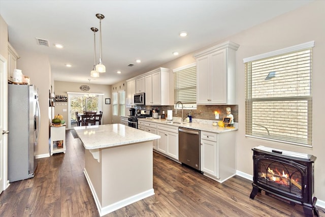 kitchen featuring appliances with stainless steel finishes, sink, decorative light fixtures, a center island, and white cabinetry