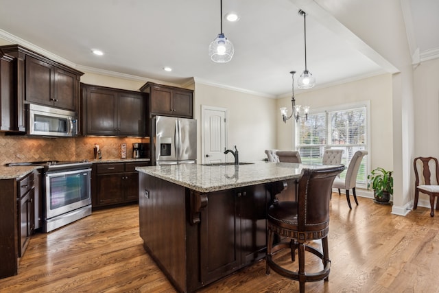 kitchen featuring decorative light fixtures, a kitchen island with sink, appliances with stainless steel finishes, and light hardwood / wood-style flooring