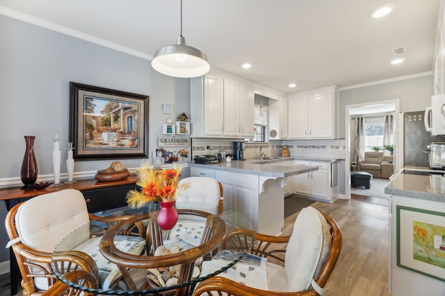 kitchen with white cabinets, pendant lighting, light hardwood / wood-style flooring, and crown molding