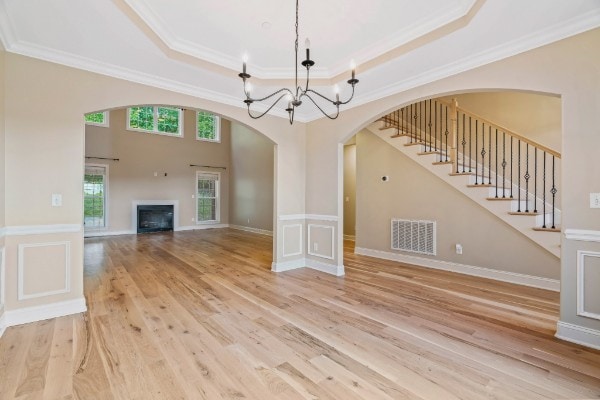 unfurnished living room with an inviting chandelier, wood-type flooring, crown molding, and a tray ceiling