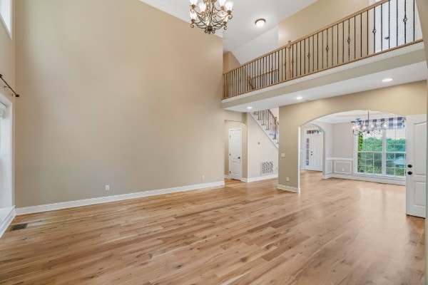 unfurnished living room with wood-type flooring, a towering ceiling, and a chandelier