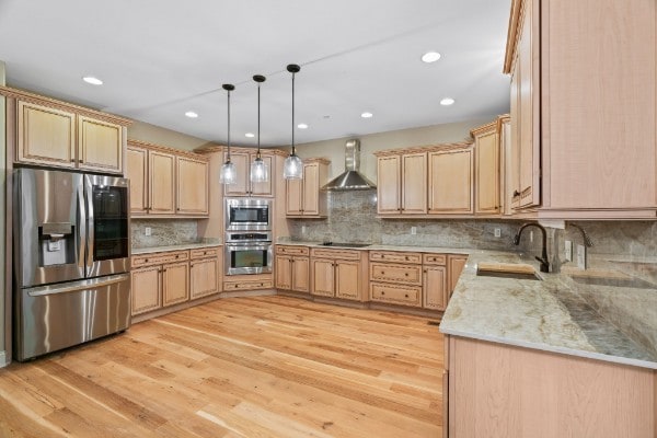 kitchen with sink, wall chimney exhaust hood, light wood-type flooring, appliances with stainless steel finishes, and decorative light fixtures