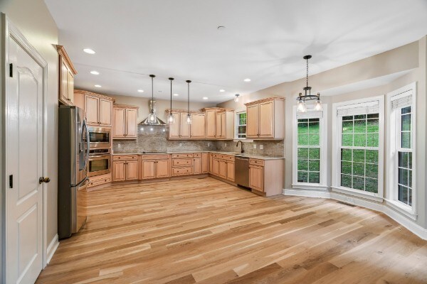 kitchen featuring pendant lighting, light brown cabinets, light wood-type flooring, appliances with stainless steel finishes, and tasteful backsplash