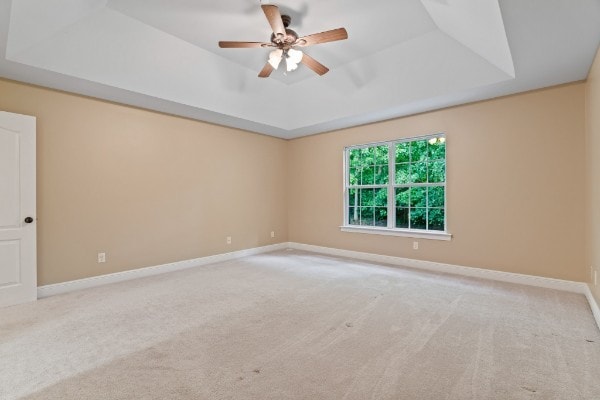 carpeted spare room featuring a tray ceiling and ceiling fan