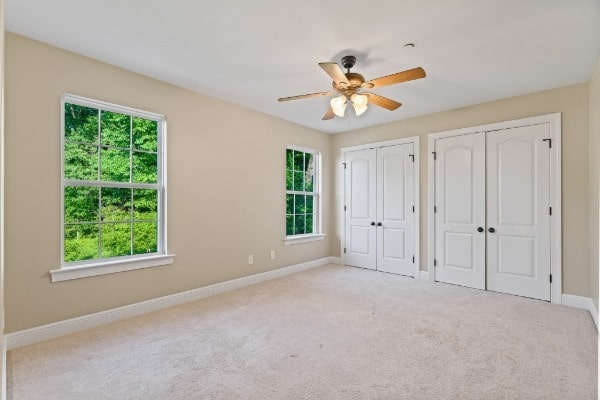 unfurnished bedroom with ceiling fan, light colored carpet, and two closets