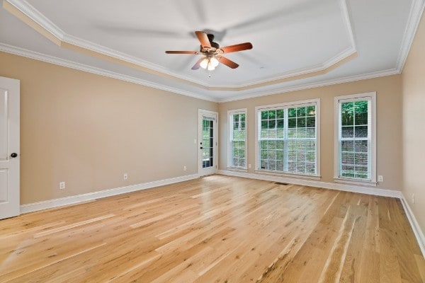 empty room with ornamental molding, light hardwood / wood-style floors, ceiling fan, and a tray ceiling