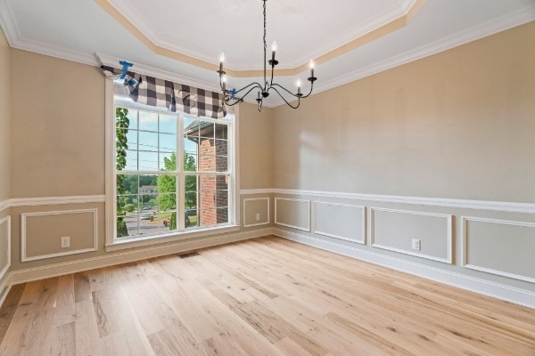 spare room featuring a tray ceiling, crown molding, hardwood / wood-style floors, and a chandelier