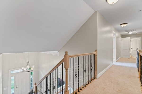 hall featuring a notable chandelier, light colored carpet, and lofted ceiling