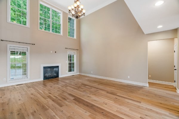 unfurnished living room featuring an inviting chandelier, a high ceiling, and light wood-type flooring