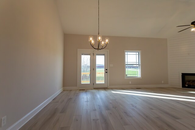 doorway featuring a large fireplace, ceiling fan with notable chandelier, and light hardwood / wood-style flooring