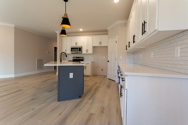 kitchen featuring a center island with sink, light wood-type flooring, pendant lighting, stainless steel appliances, and white cabinets