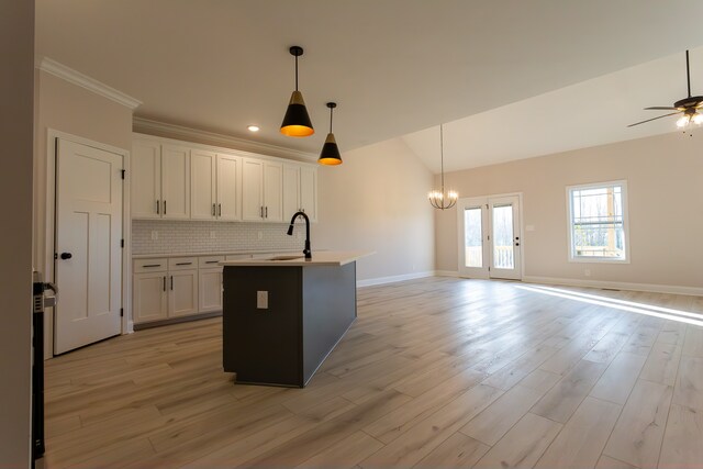 kitchen with sink, hanging light fixtures, an island with sink, decorative backsplash, and white cabinets