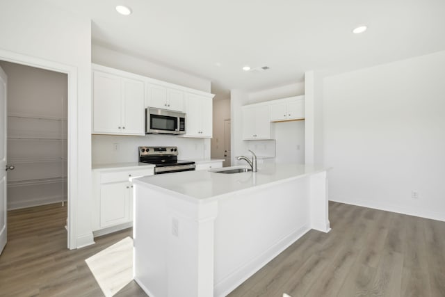 kitchen featuring white cabinetry, a center island with sink, stainless steel appliances, and light wood-type flooring