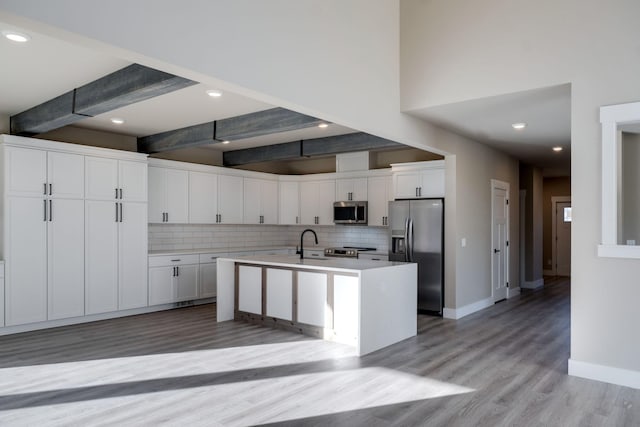 kitchen with appliances with stainless steel finishes, sink, beam ceiling, white cabinets, and an island with sink