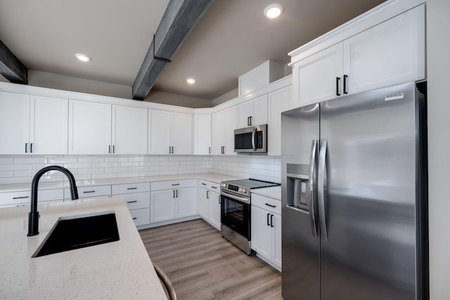 kitchen with sink, light stone countertops, beamed ceiling, white cabinetry, and stainless steel appliances