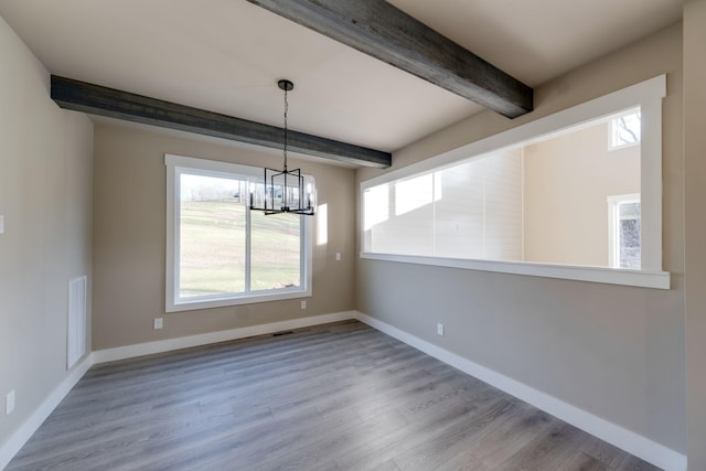 unfurnished dining area with a wealth of natural light, beamed ceiling, and light wood-type flooring