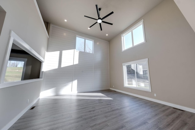 unfurnished living room with ceiling fan, a healthy amount of sunlight, a high ceiling, and light wood-type flooring