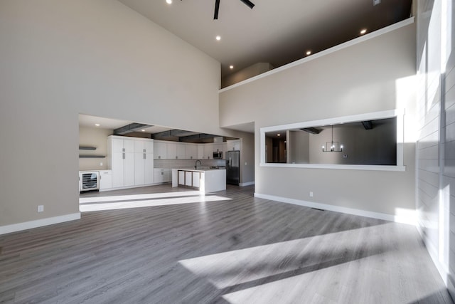 unfurnished living room with sink, beverage cooler, a high ceiling, light hardwood / wood-style flooring, and ceiling fan with notable chandelier