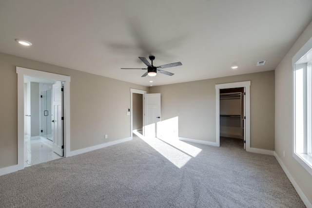 unfurnished bedroom with ceiling fan, ensuite bathroom, a walk in closet, light carpet, and a closet