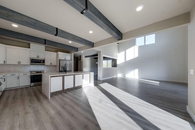 kitchen with stainless steel appliances, a kitchen island, beamed ceiling, white cabinets, and light wood-type flooring