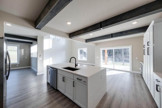 kitchen with appliances with stainless steel finishes, sink, beamed ceiling, white cabinets, and an island with sink