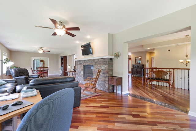 living room with a stone fireplace, ceiling fan with notable chandelier, and hardwood / wood-style flooring