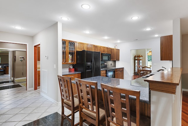 kitchen with black appliances, a kitchen breakfast bar, decorative backsplash, light tile patterned floors, and kitchen peninsula