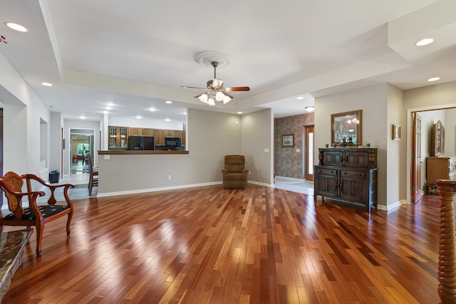 living room with hardwood / wood-style flooring, a raised ceiling, and ceiling fan