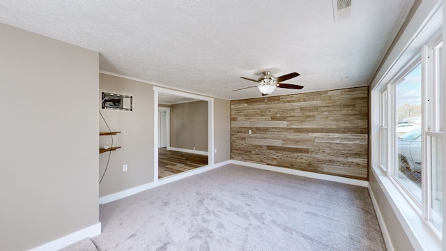 carpeted empty room with ornamental molding, a textured ceiling, ceiling fan, and wooden walls