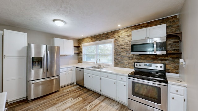 kitchen with appliances with stainless steel finishes, a textured ceiling, sink, white cabinets, and light hardwood / wood-style floors