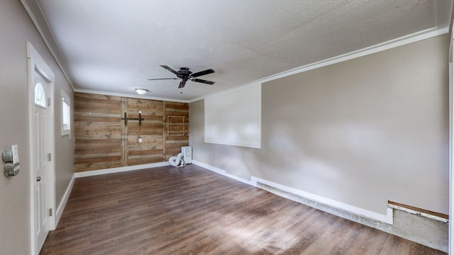 empty room with ceiling fan, dark hardwood / wood-style floors, crown molding, a textured ceiling, and wooden walls