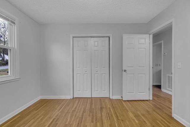 unfurnished bedroom with light wood-type flooring, a textured ceiling, and a closet