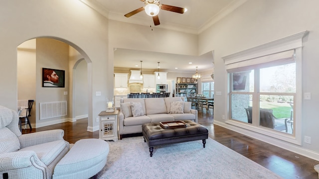 living room with crown molding, a towering ceiling, dark wood-type flooring, and ceiling fan with notable chandelier