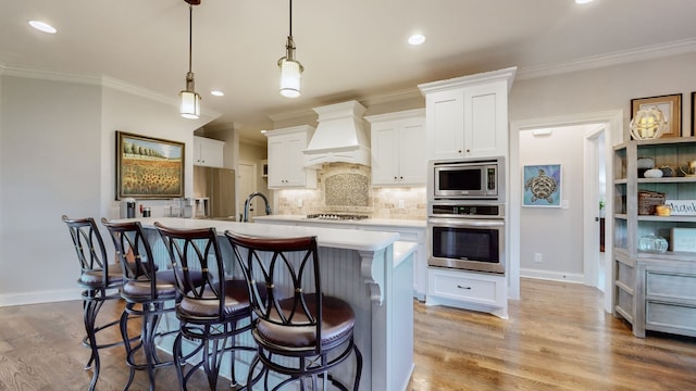 kitchen featuring custom range hood, stainless steel appliances, white cabinetry, and an island with sink