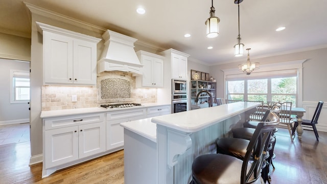 kitchen featuring pendant lighting, white cabinets, a center island with sink, and light hardwood / wood-style flooring