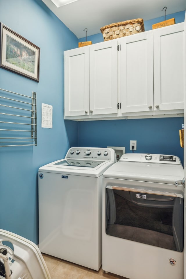 clothes washing area with washing machine and clothes dryer, light tile patterned floors, and cabinets