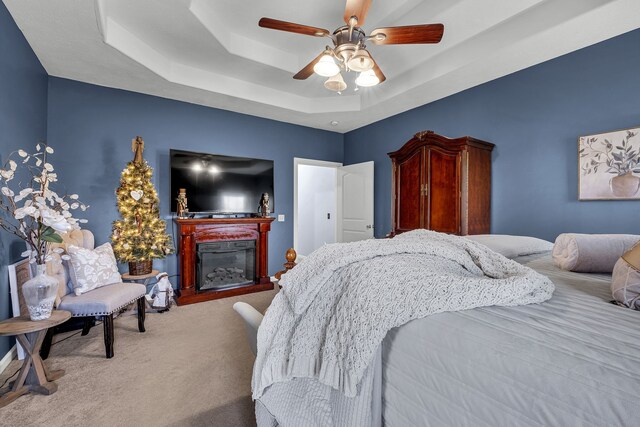 carpeted bedroom featuring a tray ceiling and ceiling fan