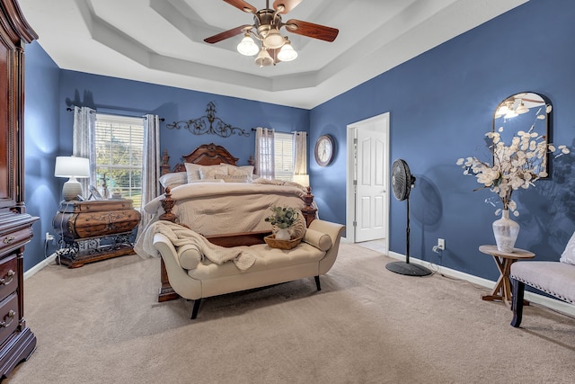 carpeted bedroom with a raised ceiling, multiple windows, and ceiling fan