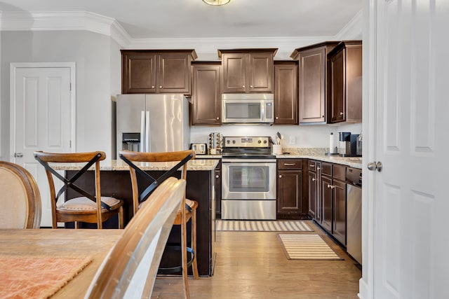 kitchen featuring dark brown cabinetry, light wood-type flooring, a breakfast bar, appliances with stainless steel finishes, and ornamental molding