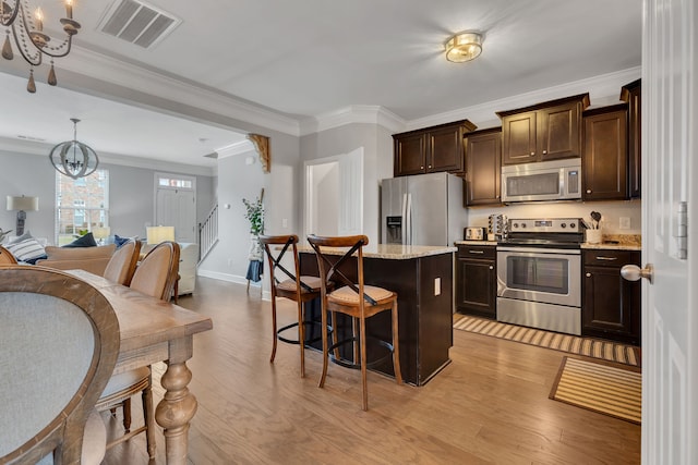 kitchen with ornamental molding, stainless steel appliances, a notable chandelier, light hardwood / wood-style floors, and a kitchen island