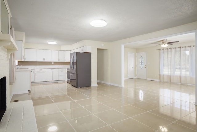 kitchen featuring stainless steel refrigerator with ice dispenser, a brick fireplace, ceiling fan, light tile patterned floors, and white cabinetry