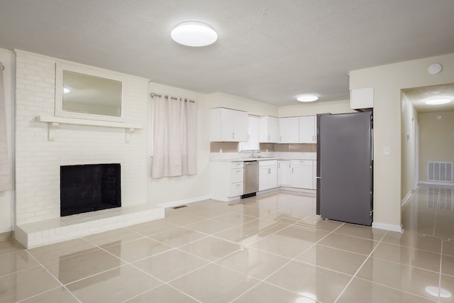 kitchen featuring white cabinetry, stainless steel appliances, a textured ceiling, a fireplace, and light tile patterned floors