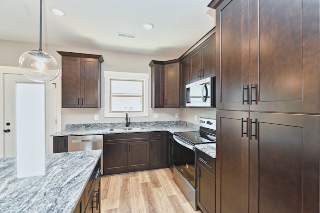 kitchen featuring light stone countertops, appliances with stainless steel finishes, sink, pendant lighting, and light hardwood / wood-style floors