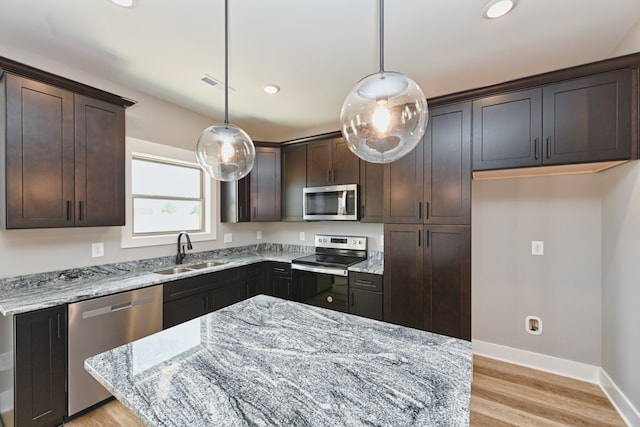 kitchen featuring hanging light fixtures, light stone countertops, sink, and stainless steel appliances