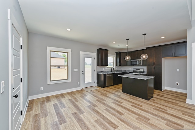 kitchen with hanging light fixtures, stainless steel appliances, dark brown cabinets, a kitchen island, and light wood-type flooring