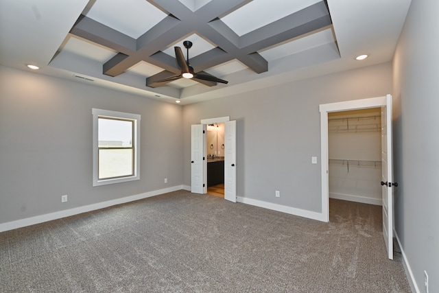 unfurnished bedroom with carpet, coffered ceiling, ceiling fan, a spacious closet, and beam ceiling