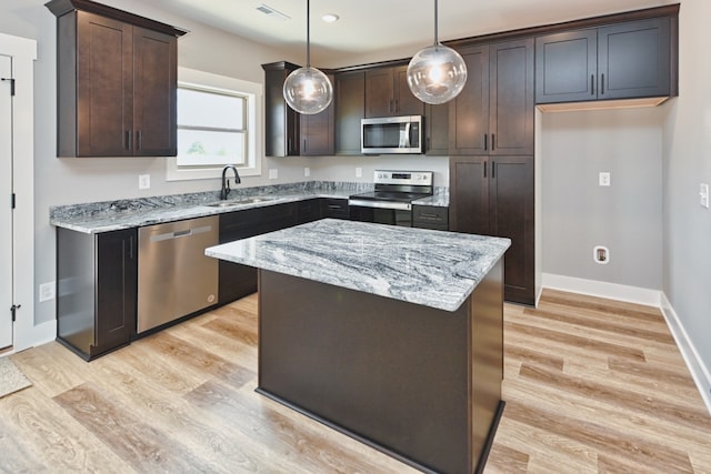 kitchen with light stone countertops, sink, decorative light fixtures, a kitchen island, and appliances with stainless steel finishes